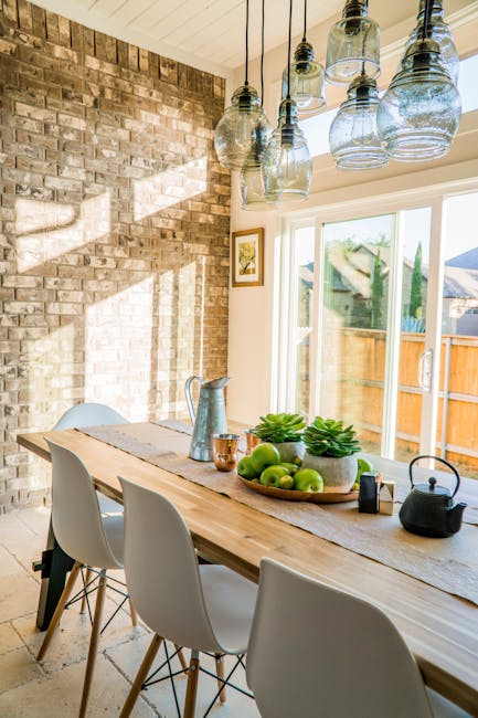 Oferta Sunlit dining room with contemporary decor and a rustic brick wall, featuring stylish lighting and a wooden table.